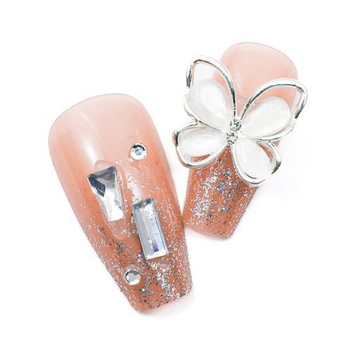 Detailed view of two pieces from a 24-piece set of handmade light pink glitter press-on coffin nails with diamond accents.