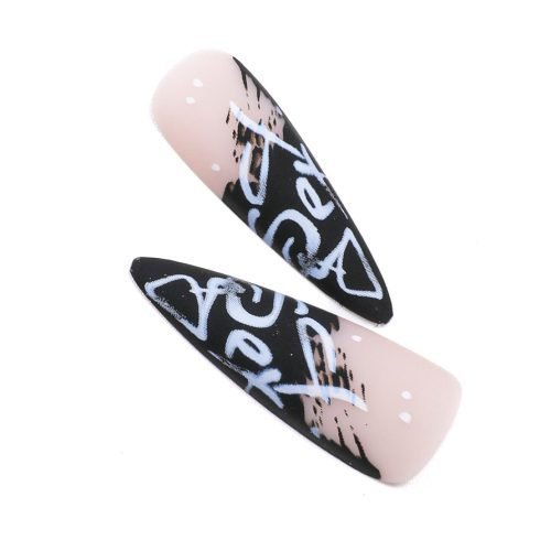 Detailed view of two pieces from a 24-piece set of black and light pink stiletto press-on nails, with bold graffiti designed nail art.