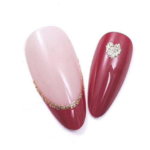 Close-up of two pieces from a set of almond-shaped press-on nails with a mix of red, golden and red-pink-golden glitter, emphasizing the French tip design.