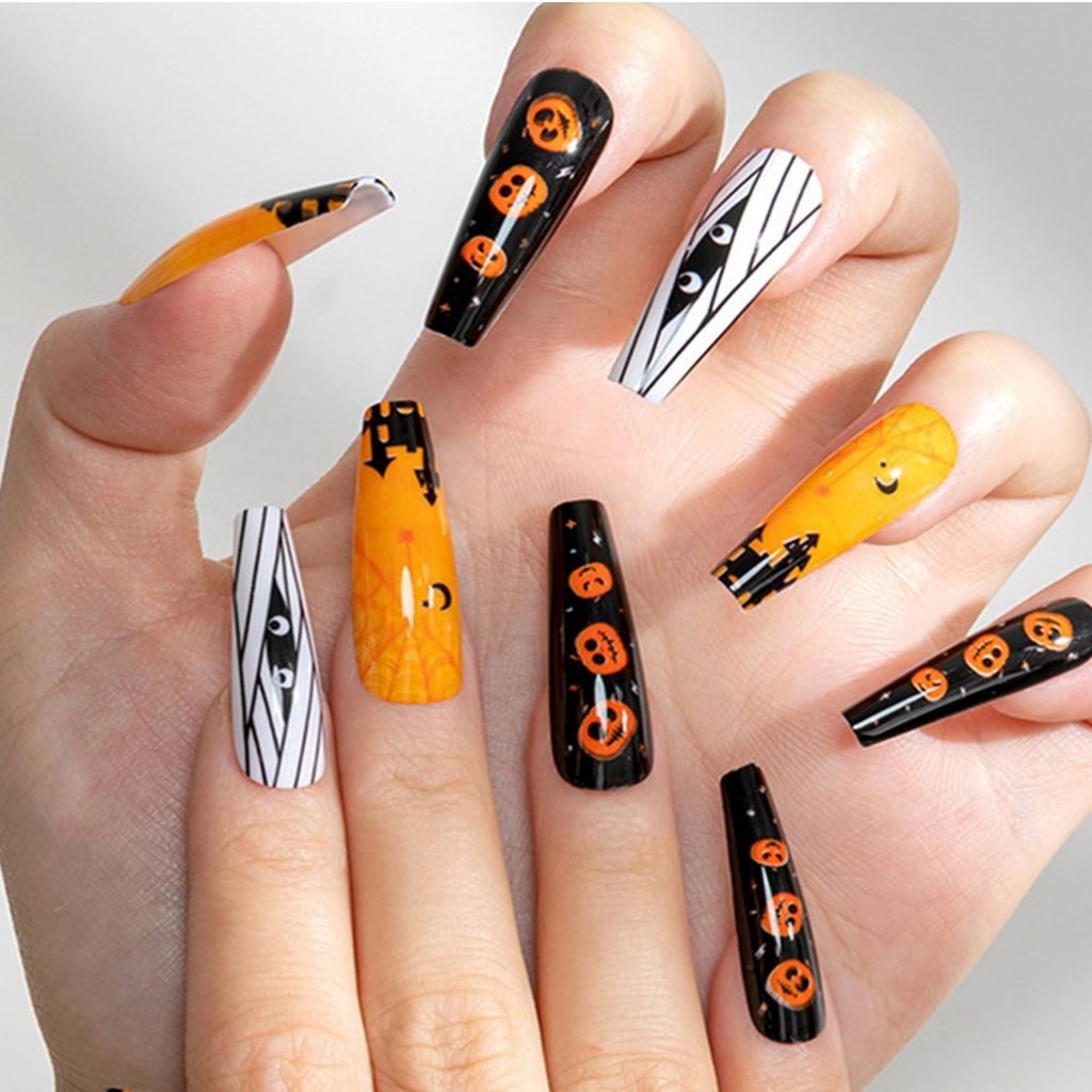 Two hands wearing a set of coffin-shaped press-on nails in orange, mixed with black and white, featuring Halloween themed designs.