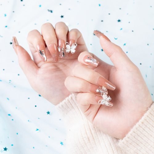 A hand displaying a set of handmade press-on coffin nails with a light pink glitter design, adorned with affixed diamonds.