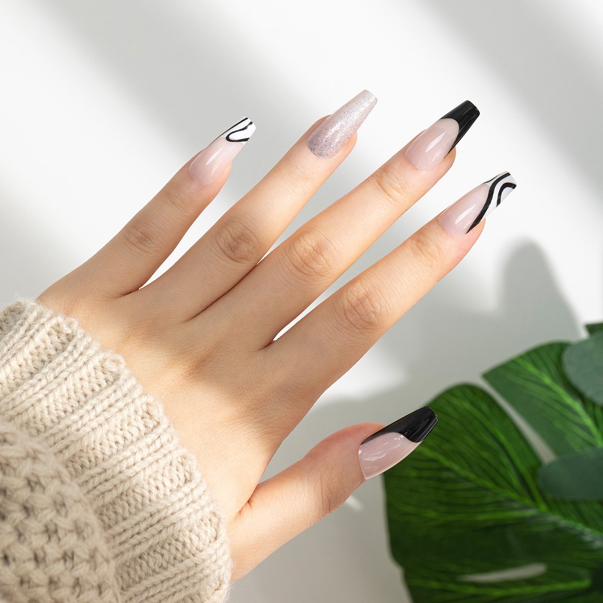 A hand showcasing a set of press-on coffin nails in a mixed design of light pink, black, and white, with a French tip.