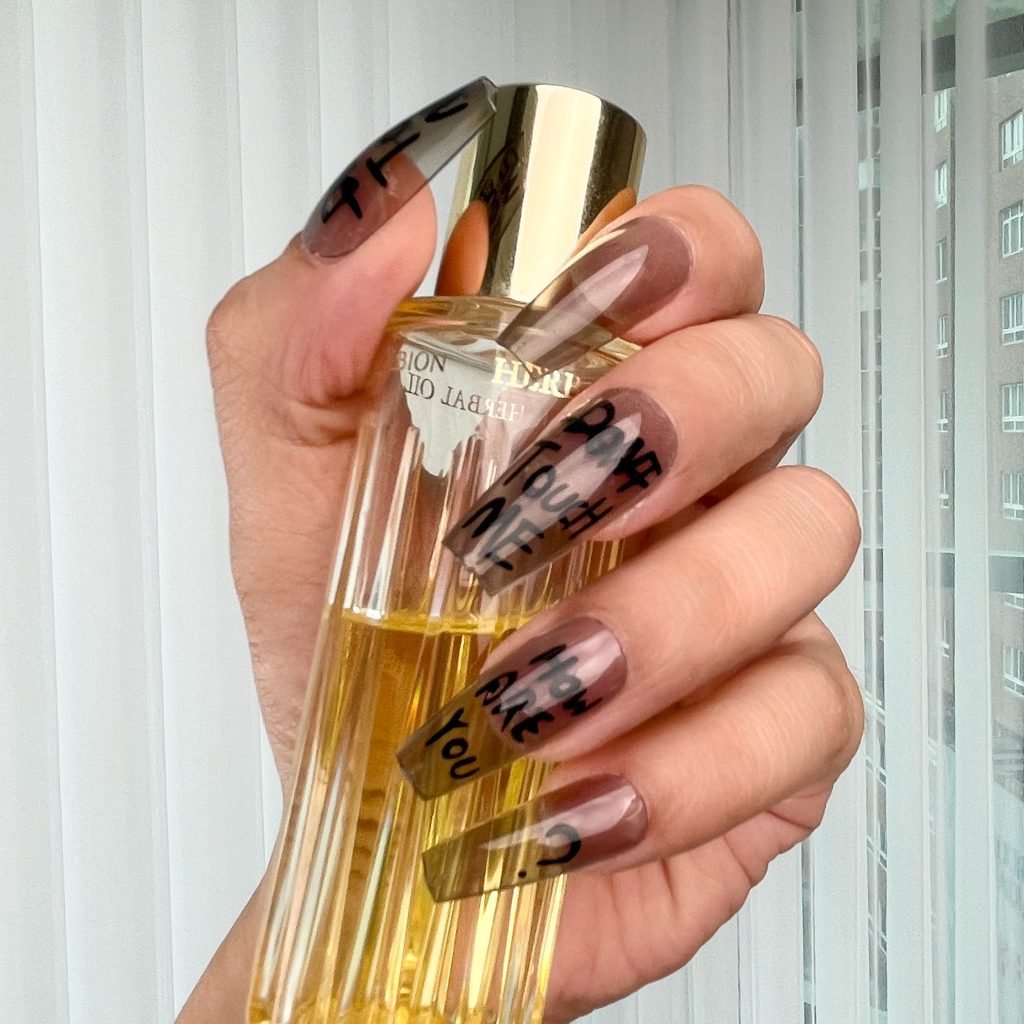 Hand with ombre gray acrylic nails holding a perfume bottle