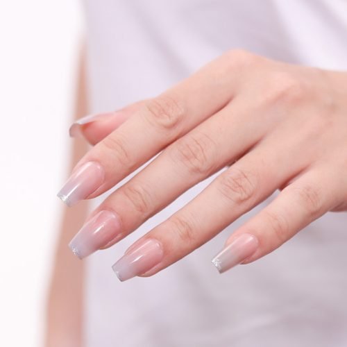 A hand stylishly flaunting a set of square press-on nails in ombre pink glass, with French tips.