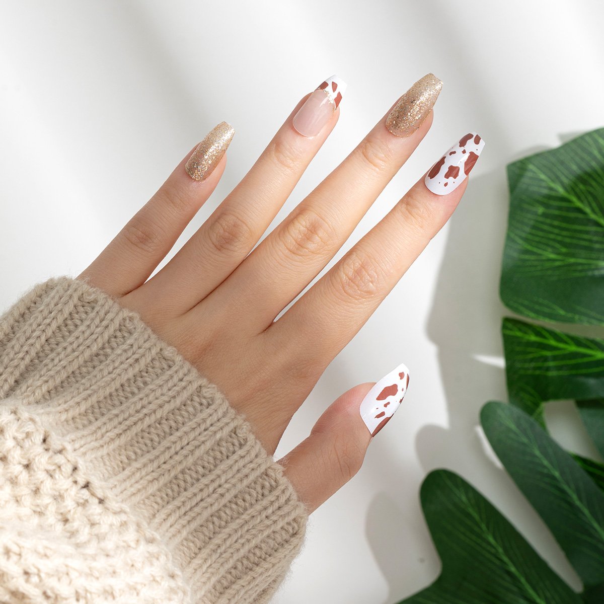 A hand showing off a set of square press-on nails in white, mixed with golden and wine red, featuring cow pattern and golden glitter.