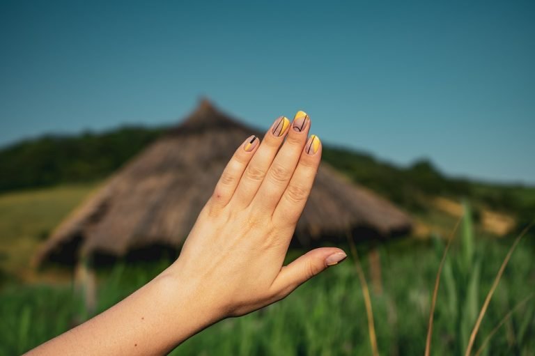 a hand wearing nude shade with yellow press-on nails, outdoor background