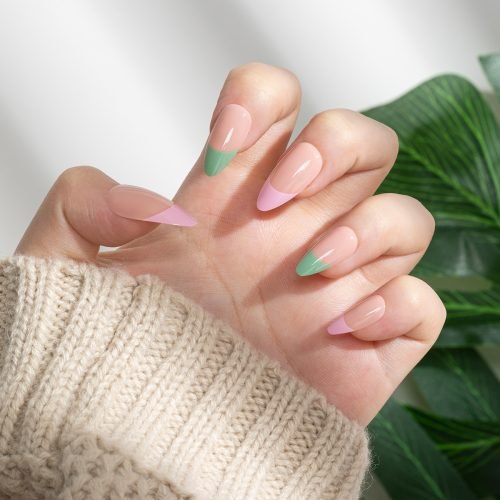 Hand wearing nude shade pop-on nails with pink and green french tip, almond shape.