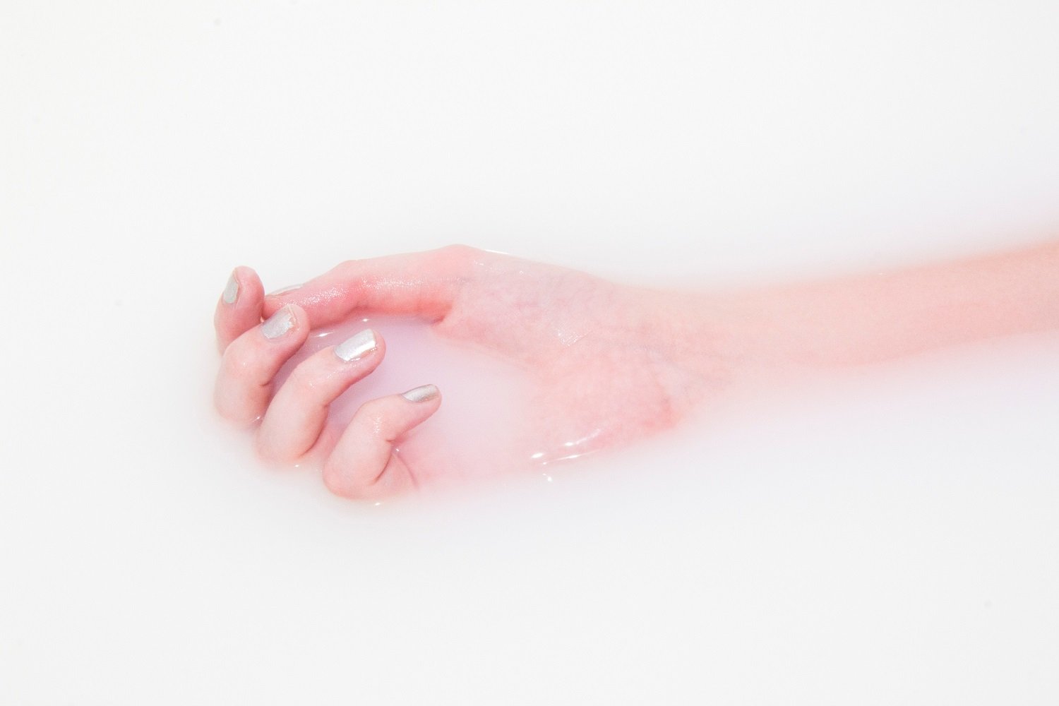 Hand with shimmery silver nails submerged in clear water.