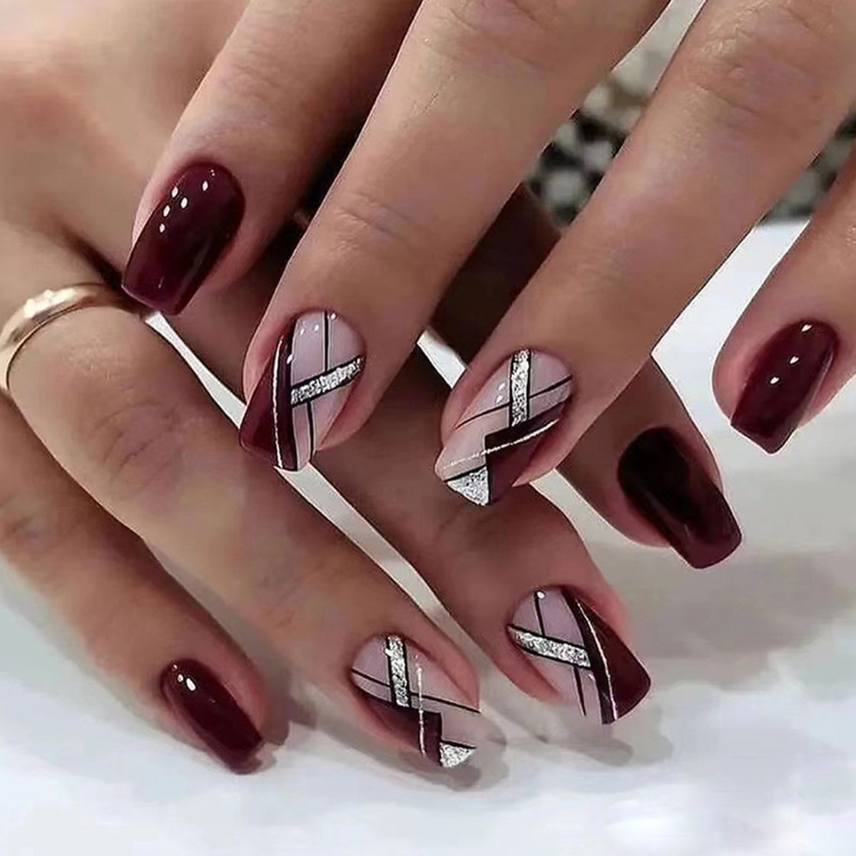 Hand showcasing square-shaped press-on nails in two styles: pure wine red shade and pink with wine red and silver glitter bars.