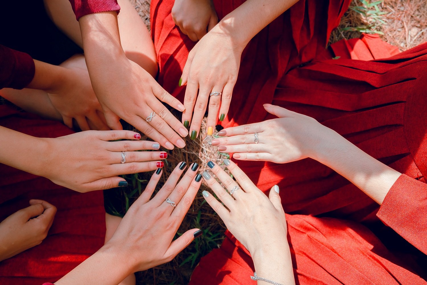 Six hands of diverse women displaying a range of colorful nail polishes.