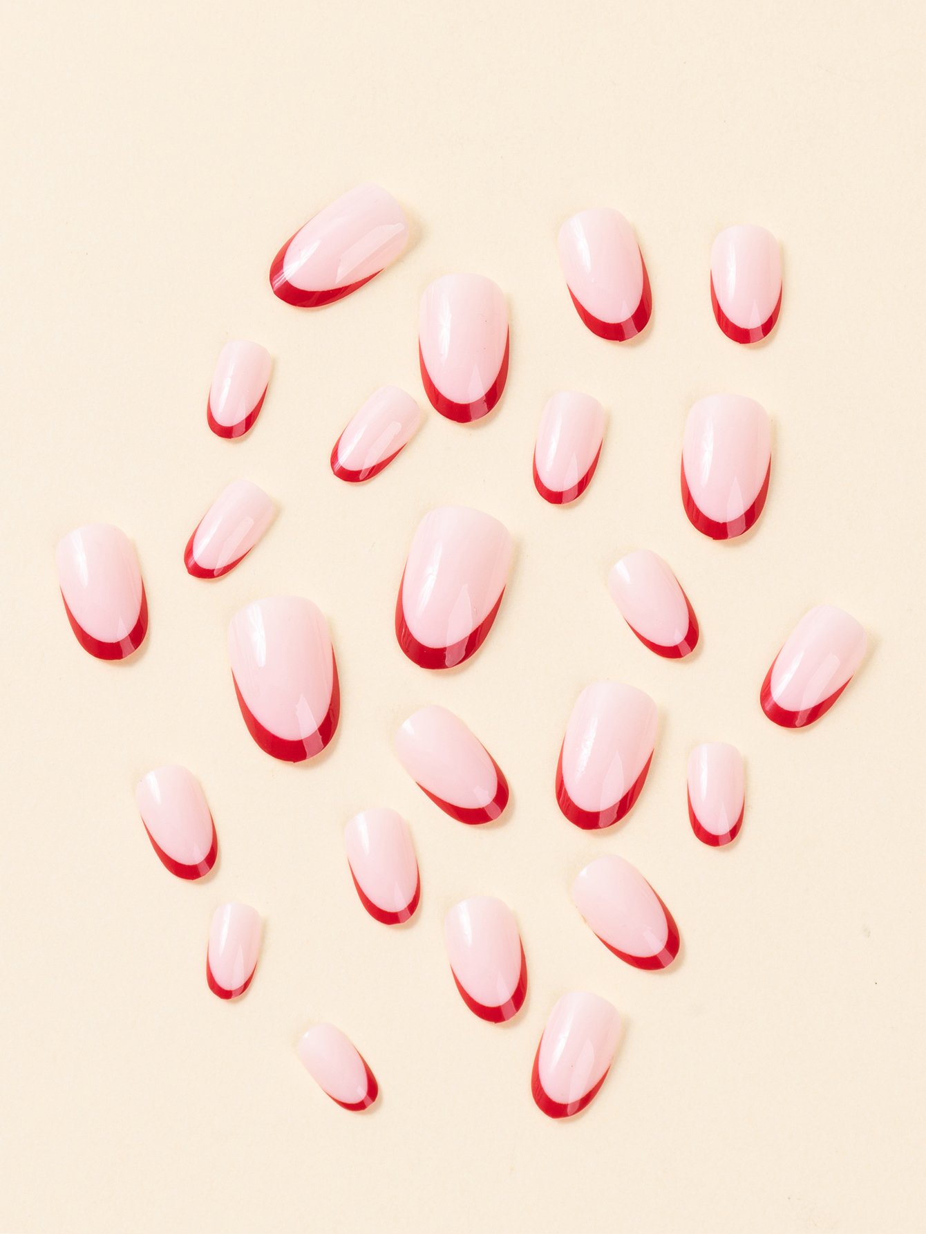 Top-down view of a 24-piece set of short almond-shaped press-on nails with nude bases and red French tips.