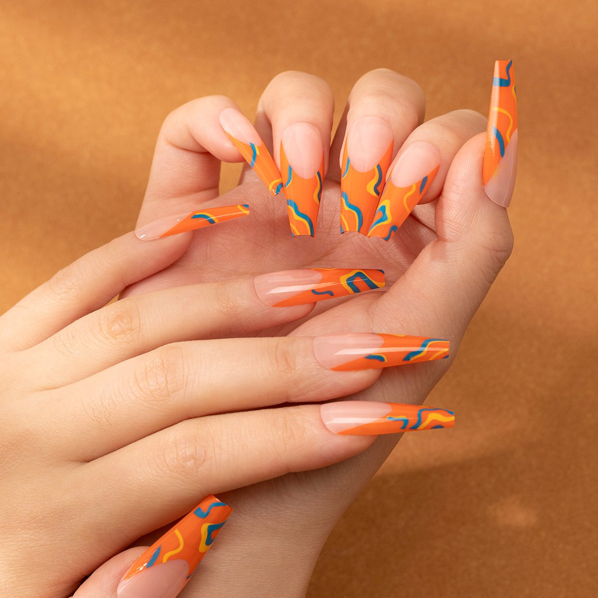 Two hands wearing long coffin-shaped stick-on nails with orange French tips accented by yellow and blue bars.