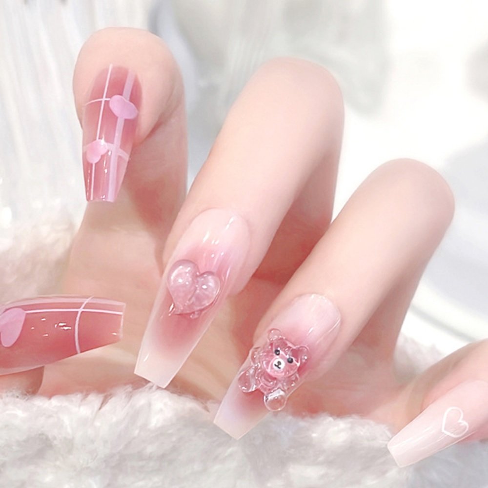 Hand adorned with coffin press-on nails, featuring designs of ombre red with heart prints and nude shade accented with gel bear embellishments.