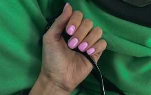 A hand flaunting pink press-on nails against a contrasting green background.