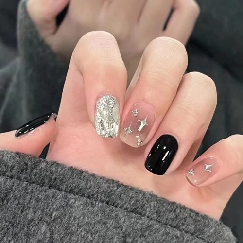 Hand showcasing squoval press-on nails in designs of solid black, ombre red with diamond accessories, and glitter dip accented with diamonds.