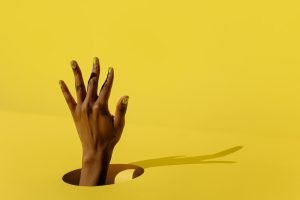 A hand with yellow press-on nails against a matching yellow background.